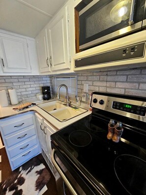 A kitchen with white cabinets, a microwave, a stove, a sink, and a coffee maker.