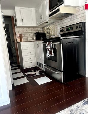 Una cocina compacta con armarios blancos, horno de acero inoxidable y microondas.