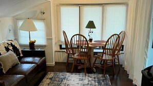A living room with a brown leather sofa, a dining table with chairs, a patterned rug, and a window with curtains. - Cozy Riverfront RV Retreat with Seasonal Pool & Trout Fishing near Hiawassee, Georgia (Hiawassee)