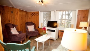 Ein Zimmer mit Holzwänden, zwei Sessel, einem Fernseher, einem kleinen Tisch und einer Lampe.
