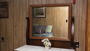 Ein Zimmer mit Holzwänden, einem großen Spiegel, einem Nachttisch mit Blumen und einem Bett mit Kissen.