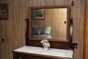 Ein Zimmer mit Holzwänden, einem großen Spiegel, einem Nachttisch mit Blumen und einem Bett mit Kissen.