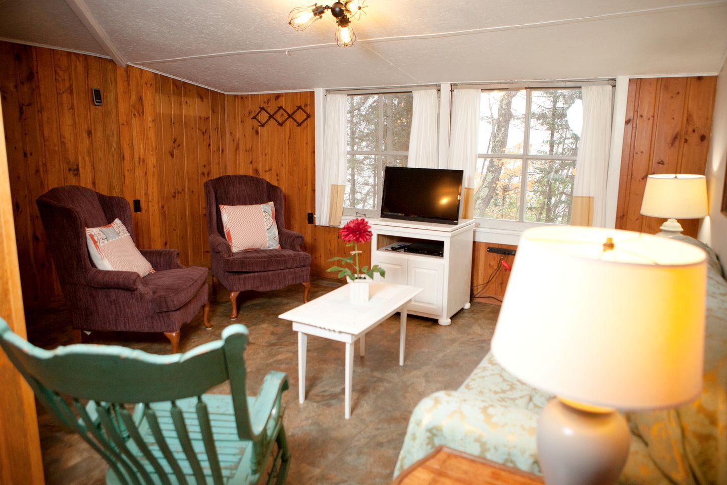 A room with wooden walls, two armchairs, a television, a small table, and a lamp.
