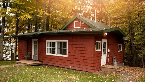 Eine kleine, eingeschossige Holzhütte mit einem grünen Dach, einer Veranda und einer Tür mit einem kleinen Fenster darüber.