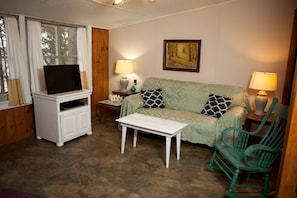 Uma sala de estar acolhedora com televisão, sofá, mesa de centro e uma poltrona.