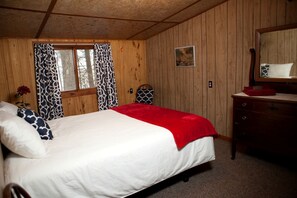 A wooden-paneled room with a bed, a dresser, a window with patterned curtains, and a painting on the wall. - Rustic Camping Cabin with a Lake View near Bayfield, Wisconsin (Ashland)