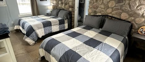 Quarto com duas camas, parede de pedra, ventoinha no teto e placa de lavanderia.