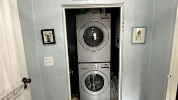 Uma lavanderia com duas máquinas de lavar empilhadas, uma placa acima da porta e um quadro na parede.