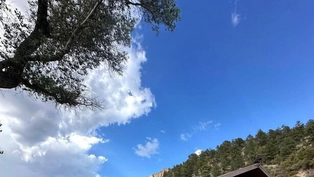 Un edificio de piedra con techo inclinado, un porche y vistas a una ladera boscosa.
