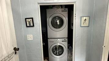 A laundry room with two stacked washing machines, a sign above the door, and a framed picture on the wall.