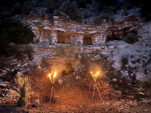 Une formation rocheuse avec une petite entrée de grotte, entourée d’une végétation désertique.
