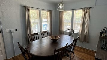 A dining area with a round wooden table, six chairs, a central bowl, and a hanging light fixture.