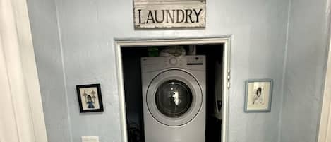 A laundry room with two stacked washing machines, a sign above the door, and a framed picture on the wall.