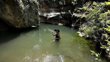 A person in a natural setting with water, surrounded by vegetation and rocky terrain.