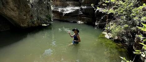 A person in a natural setting with water, surrounded by vegetation and rocky terrain.
