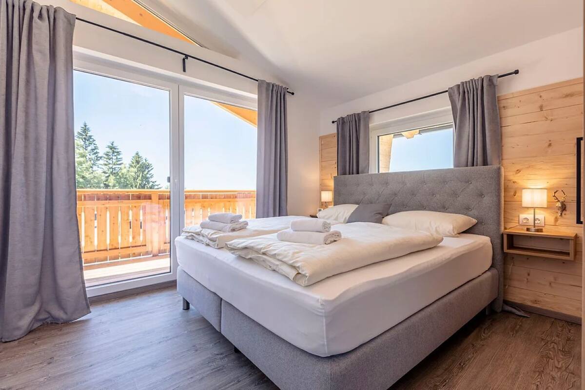 A bedroom with a large bed, a wooden headboard, a nightstand with a lamp, and a sliding glass door to a balcony.