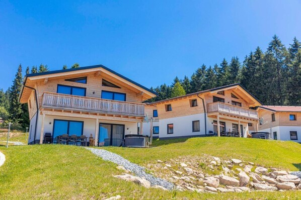 A two-story chalet with balconies, a hot tub, and a stone pathway.