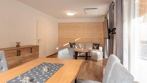 Un interior moderno con una mesa de comedor de madera, sillas tapizadas en gris, un sofá con un cojín con forma de cabeza de ciervo y un panel de pared de madera.
