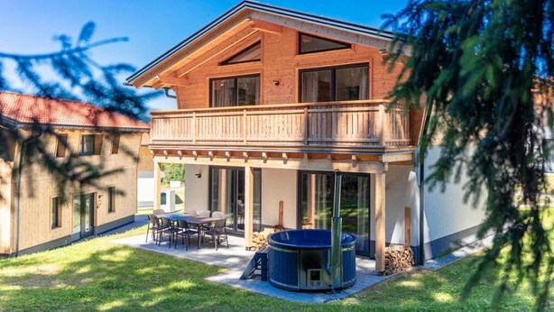 Una casa de madera de dos pisos con un balcón, un patio con mobiliario exterior y un jacuzzi.