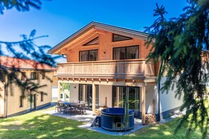 A two-story wooden house with a balcony, a patio with outdoor furniture, and a hot tub.