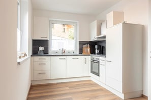 A modern kitchen with white cabinets, a window, and a built-in oven.