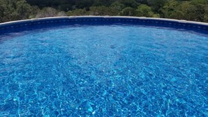 A clear blue swimming pool with a view of a forested landscape.