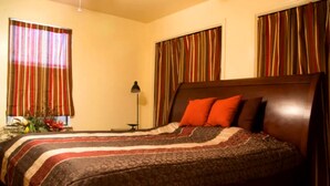 A hotel room with a bed, curtains, a lamp, and a nightstand.