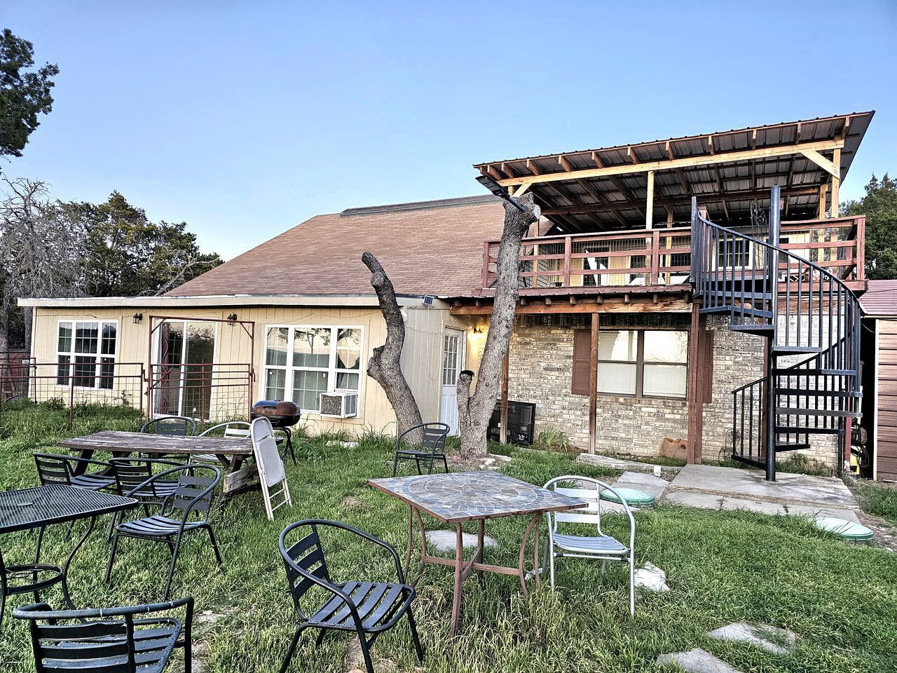 A rustic building with a wooden deck, outdoor seating, and a spiral staircase.