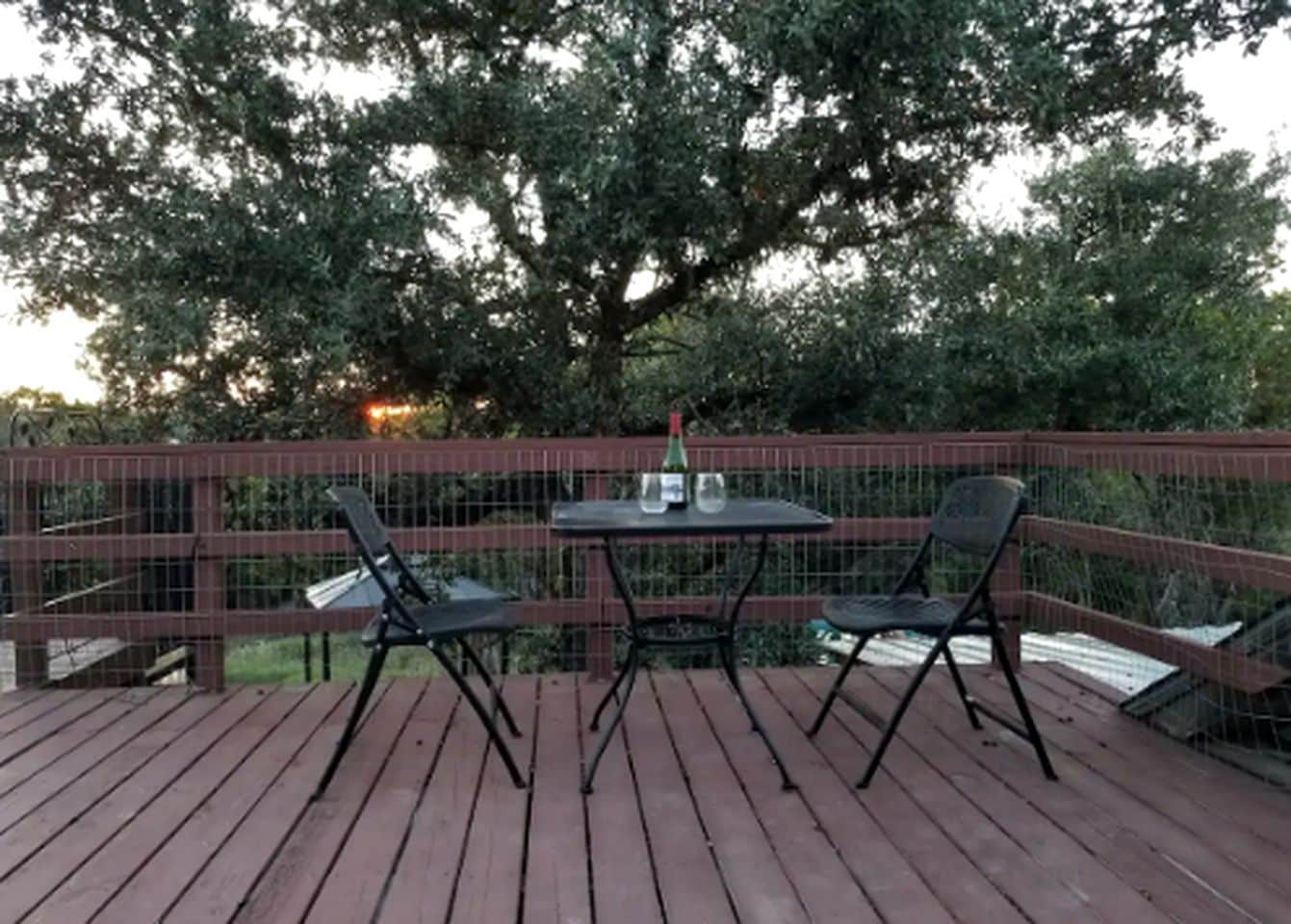 A wooden deck with a table and two chairs, surrounded by a metal fence.