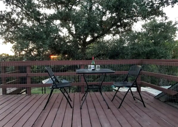 A wooden deck with a table and two chairs, surrounded by a metal fence.
