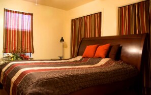A hotel room with a bed, curtains, a lamp, and a nightstand.
