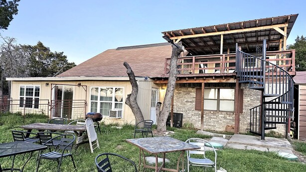 Un edificio rústico con terraza de madera, mobiliario exterior y una escalera en espiral.