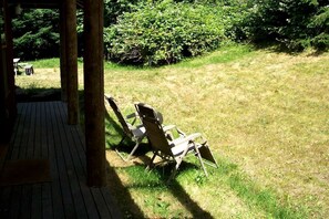 Une terrasse en bois avec deux chaises longues donnant sur une zone herbeuse bordée d’arbustes denses.