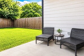 Eine Terrasse mit zwei Korbstühlen, einem kleinen runden Tisch und einem Blumentopf.