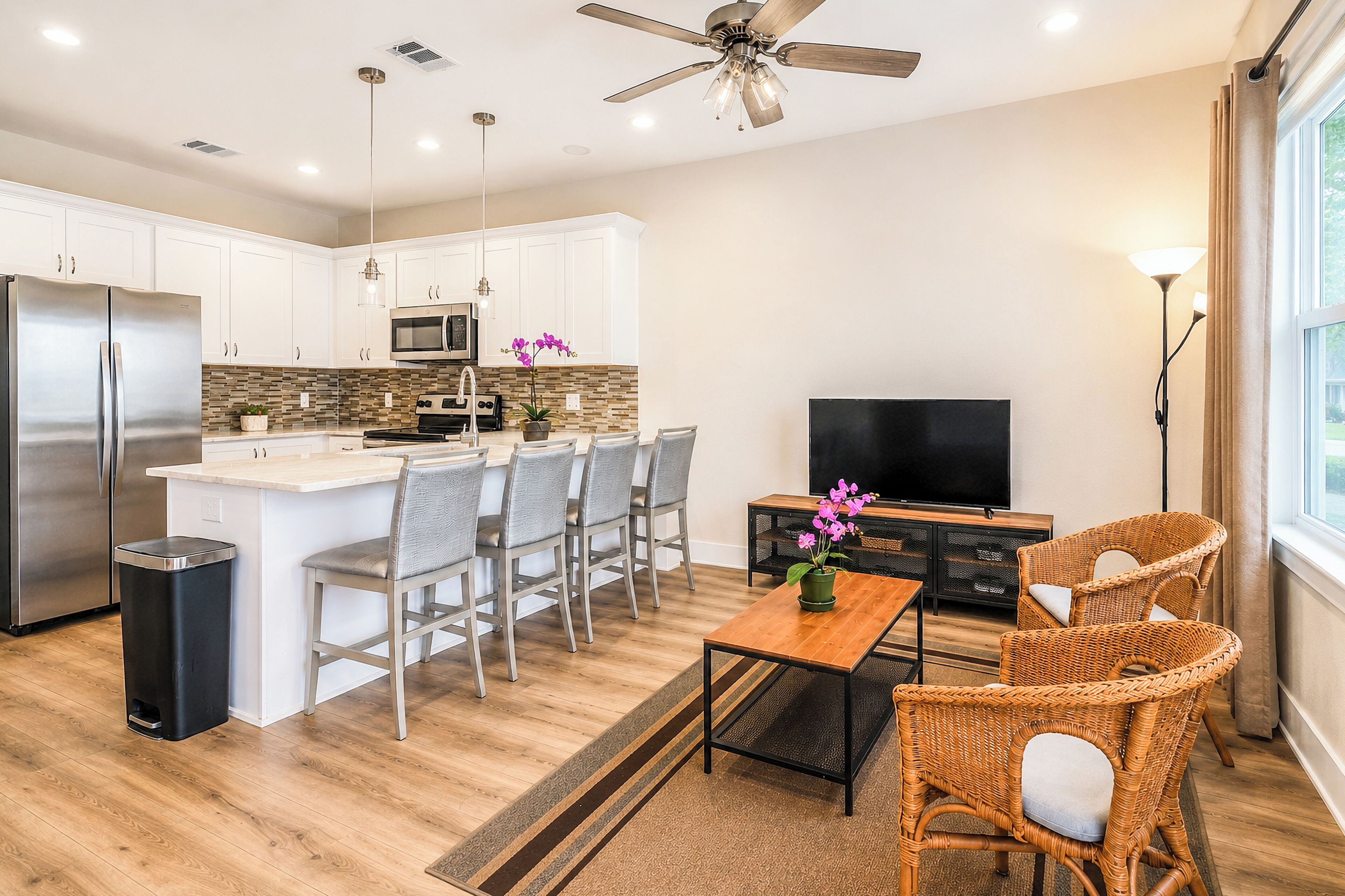 A modern kitchen with a central island, stainless steel appliances, and a dining area with wicker chairs.