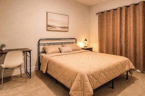 Ein Schlafzimmer mit Bett, Nachttisch, Lampe, Stuhl und einem Bild an der Wand.
