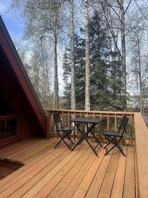 Una terraza de madera con una mesa y sillas, rodeada de árboles altos.