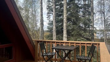 A wooden deck with a table and chairs, surrounded by tall trees.