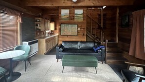 Ein Holzblockbau-Innenraum mit einer Couch, einem Esstisch und einer Küchenzeile.