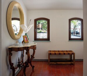 A hallway with a large mirror, a small table with a vase and picture frame, and two windows with views of the outdoors. - Villa Maline – Private country villa with a hot tub and sauna (Marche)