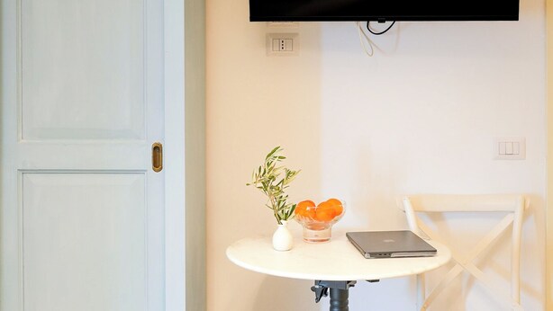 A room with a light blue wardrobe, a round table with a laptop, a chair, and a wall-mounted TV. - Villa Maline – Private Country Villa with a Jacuzzi and Sauna (Marche)