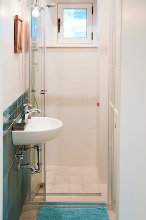 Un baño con lavabo, ducha y una ventana pequeña.