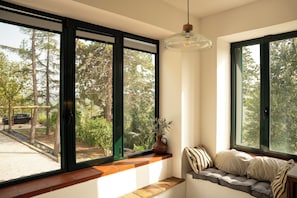 A room with large windows, a bench with cushions, and a hanging light fixture. - Villa Maline – Private Country Villa with a Jacuzzi and Sauna (Marche)