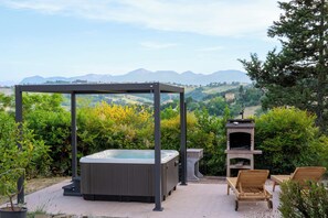 Un jacuzzi, mobiliario de jardín y una parrilla en un jardín con vistas a la montaña.