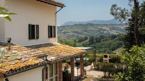 A building with a tiled roof, a garden with a pergola, and a view of rolling hills. - Villa Maline – Private Country Villa with a Jacuzzi and Sauna (Marche)