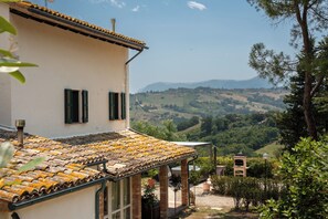 A building with a tiled roof, a garden with a pergola, and a view of rolling hills. - Villa Maline – Private Country Villa with a Jacuzzi and Sauna (Marche)