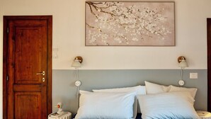 A bedroom with a wooden door, a bed with white and blue bedding, two bedside lamps, and a wall-mounted artwork of a branch with flowers. - Villa Maline – Private Country Villa with a Jacuzzi and Sauna (Marche)