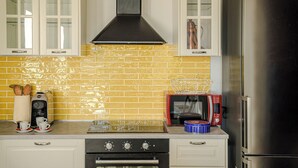 A kitchen with white cabinets, a yellow-tiled backsplash, a stainless steel range hood, a red microwave, and a black refrigerator. - Villa Maline – Private Country Villa with a Jacuzzi and Sauna (Marche)
