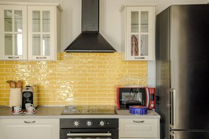 A kitchen with white cabinets, a yellow-tiled backsplash, a stainless steel range hood, a red microwave, and a black refrigerator. - Villa Maline – Private Country Villa with a Jacuzzi and Sauna (Marche)