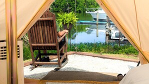 Una carpa con vistas a un lago y barcos, una silla de madera y una planta en maceta.